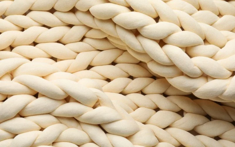 Close-up of a thick, cream-colored woven fabric with large braids, showcasing the texture of the best yarn for a chunky blanket.