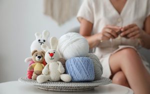 A person knitting beside a table with a tray holding the best yarn for amigurumi, along with crocheted animal toys.