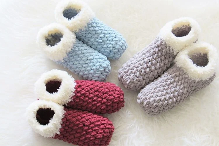 Four pairs of knitted slippers on a white fur rug.