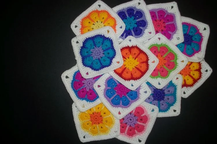 A group of colorful crocheted squares on a black surface.