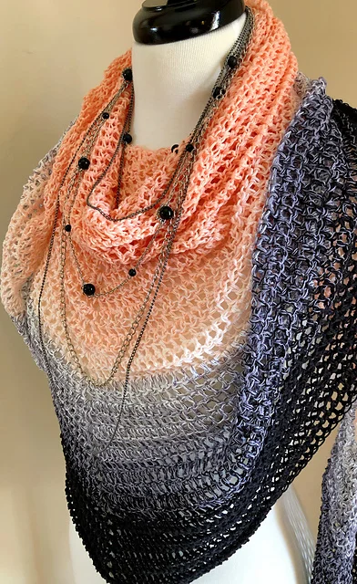A mannequin displays a Beginner Triangle Shawl in gradient peach, lavender, and black tones, accessorized with layered silver and black bead necklaces.