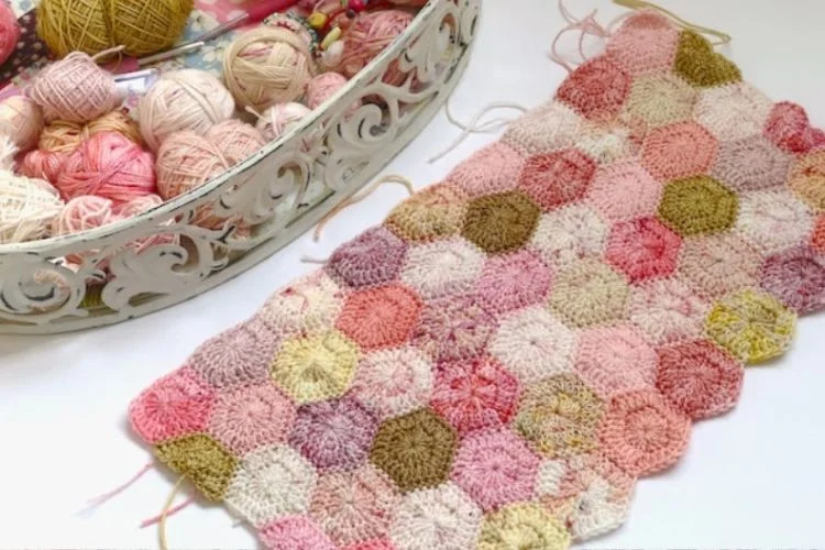 A crocheted hexagon afghan on a table next to a basket of yarn.