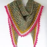 A multicolored Spindle Shawl with a lacy texture, featuring green and yellow tones and finished with pink and red scalloped edging, hangs on a white hanger.
