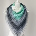 A mannequin displays a Beginner One Skein Shawl, crocheted in a triangular shape with gradient colors ranging from white to mint green to dark gray.