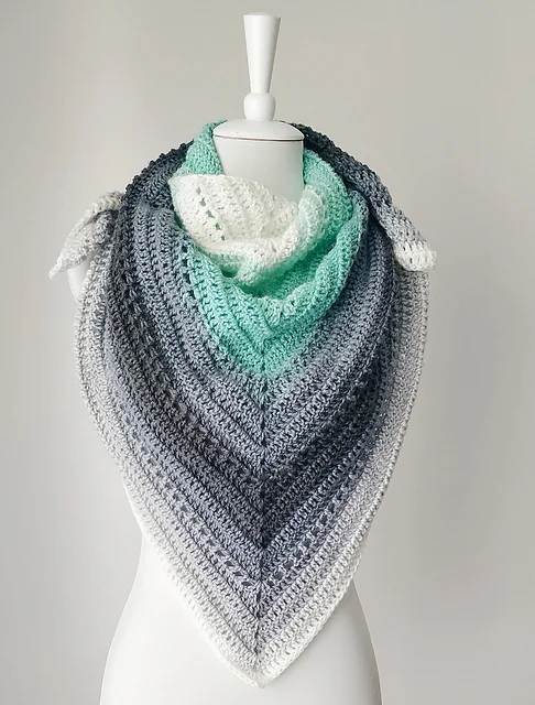 A mannequin displays a Beginner One Skein Shawl, crocheted in a triangular shape with gradient colors ranging from white to mint green to dark gray.