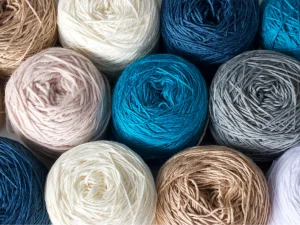 A neat pattern showcases various balls of yarn in shades of blue, beige, white, and gray—perfect picks when deciding what yarn to use for crochet projects.