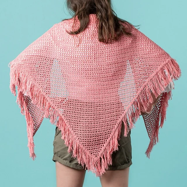 Person wearing a pink, fringed Summerday Shawl draped over their shoulders, standing against a blue background, facing away from the camera.