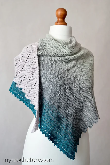 The Willow Shawl is a knitted shawl with a gradient color transition from light gray to teal, beautifully displayed on a white mannequin torso.