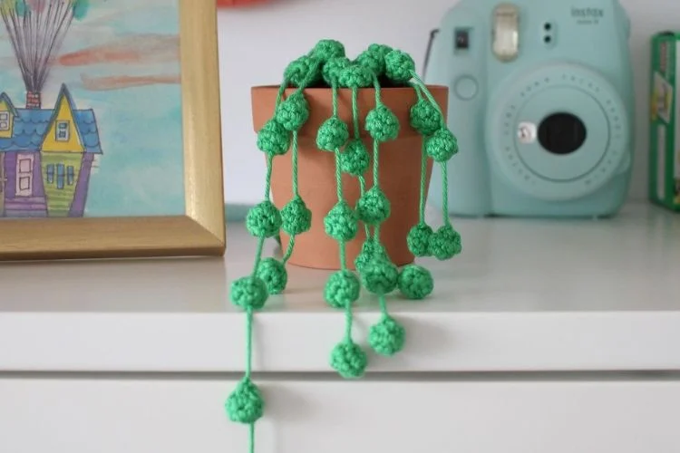 Green crocheted balls hanging from a pot on a dresser.