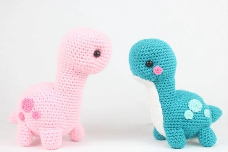 Two crocheted dinosaurs sitting next to each other.