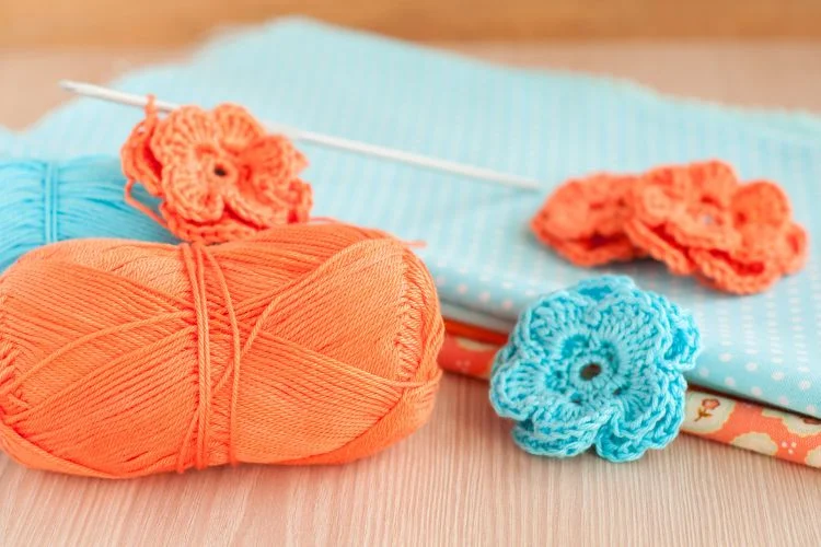 Crocheted flowers and yarn on a wooden table demonstrating how to crochet a circle.