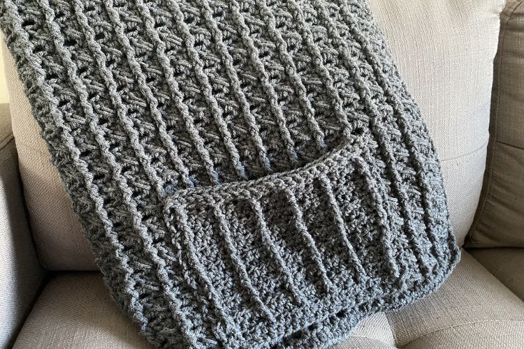 A grey crocheted blanket sitting on a couch.