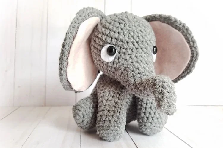 A gray crocheted elephant stuffed animal sitting on a wooden floor.