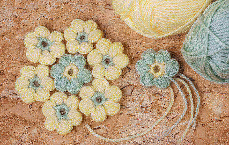 Crochet flowers in vibrant yellow and green are artfully arranged on the surface, accompanied by two inviting balls of yarn.