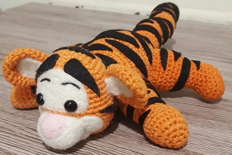 A crocheted tiger laying on a wooden floor.