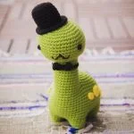 a crochet brontosaurs dinosaur amigurumi wearing a black hat and a tie bow