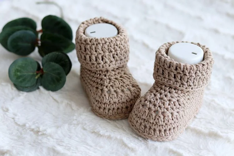 A pair of crocheted baby booties atop a white blanket.