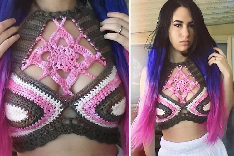 A woman with pink and purple hair is wearing a crocheted top.