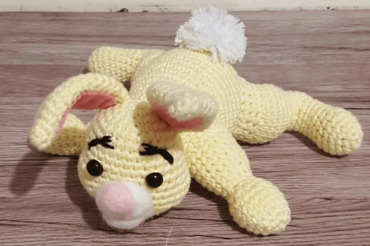 A crocheted bunny laying on a wooden floor.