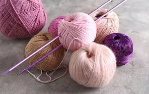 Balls of yarn in various colors, showcasing different yarn weights, lie alongside two knitting needles on a gray surface.