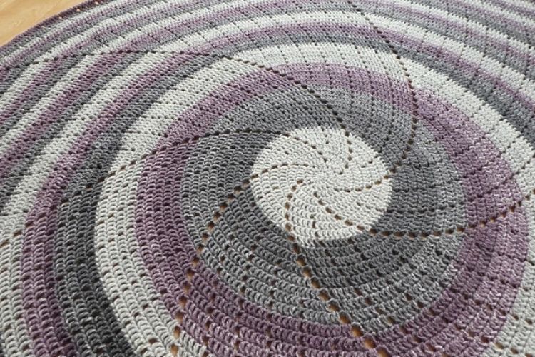 A purple and white crocheted rug on a wooden floor.