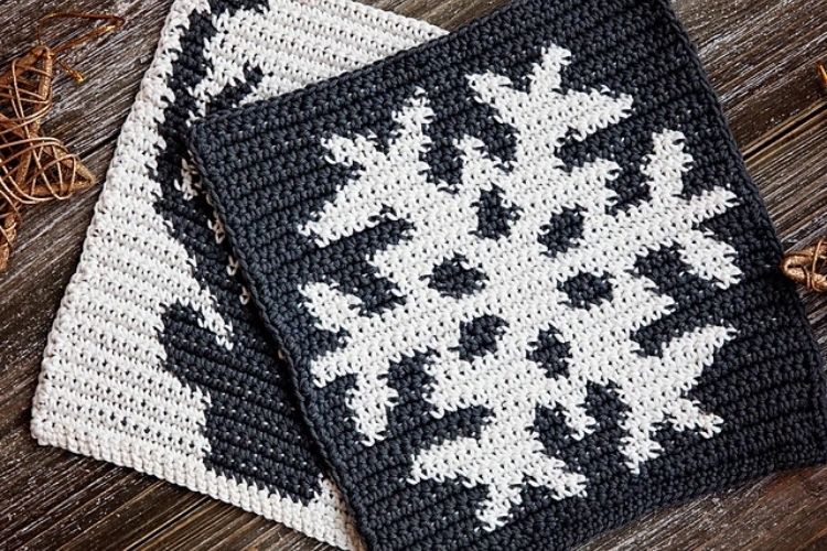 Two crocheted snowflake dishcloths on a wooden table.