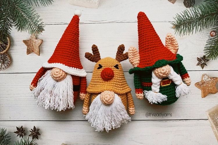 Three crocheted gnomes sitting on a christmas tree.