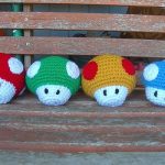 Four crocheted nintendo mario amigurumi dolls sitting on a bench.