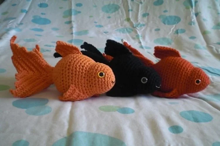 Three crocheted goldfish sitting on a bed.