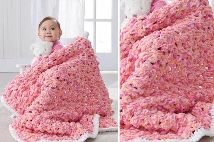 A baby is holding a pink crocheted afghan.