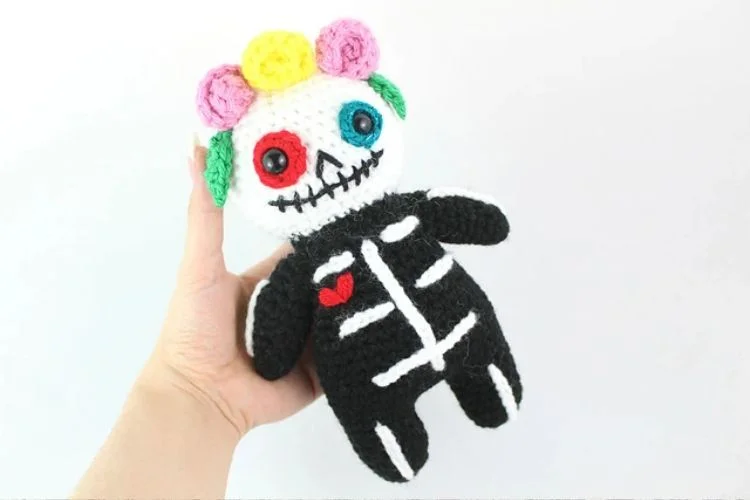 A hand holding a crocheted sugar skull doll.