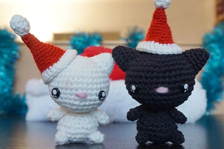 Two crocheted black and white cats wearing santa hats.