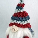 A handmade Christmas Gnome—Amigurumi Crochet Pattern—with a striped red, blue, and gray hat, white beard, and round nose, set against a plain background.
