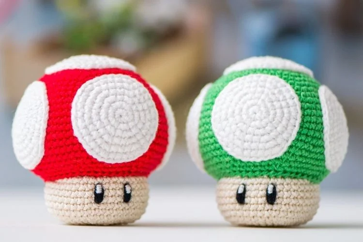 Two crocheted nintendo mario toys on a table.