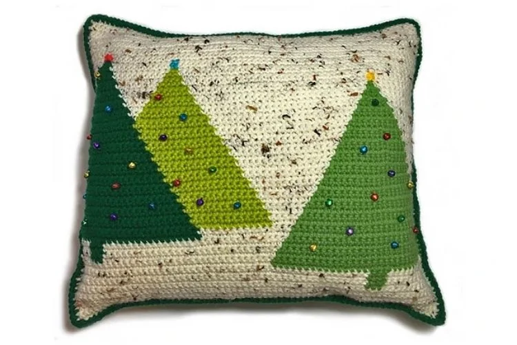 A crocheted pillow with christmas trees on it.