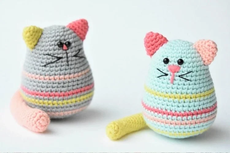 Two crocheted cats sitting next to each other.