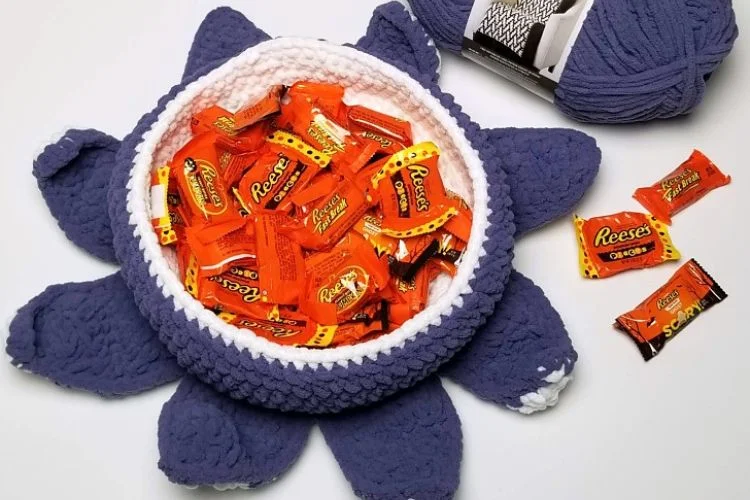 A crocheted bowl filled with candy and yarn.