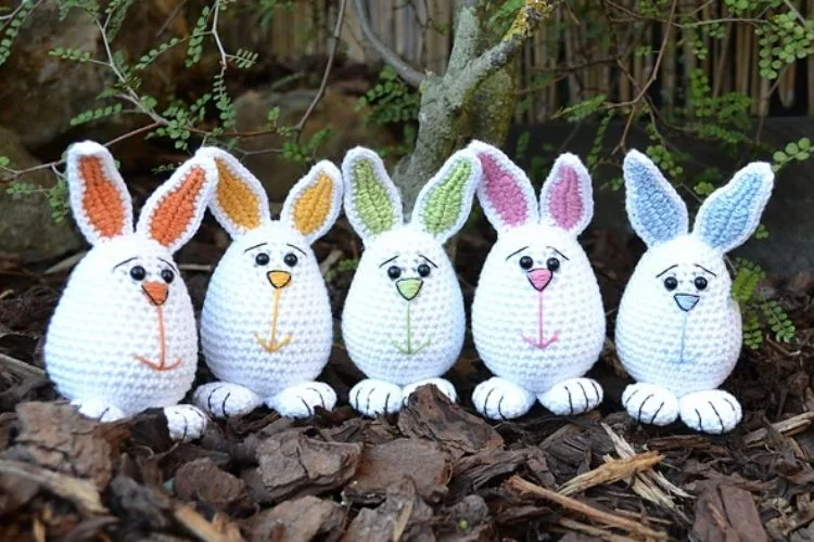 Four crocheted bunnies sitting in a pile of leaves.