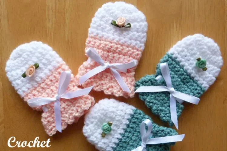 Four crocheted mittens with bows on them.