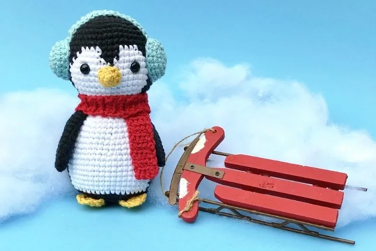 A crocheted penguin sits next to a sled.