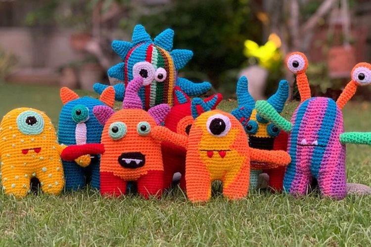 A group of crocheted monsters sitting on the grass.