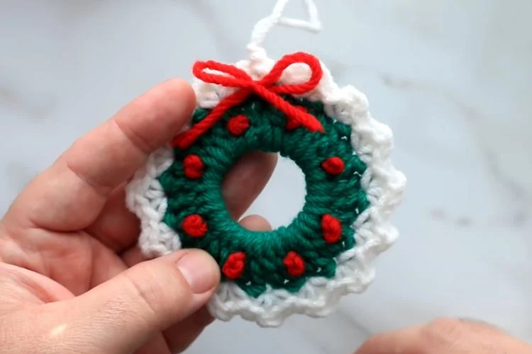 A person holding a crocheted christmas wreath ornament.