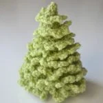 A small, light green, crocheted Christmas Tree is displayed on a plain white background.