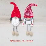 Two crocheted Danish Christmas Gnome dolls sit on concrete steps, each with long hats—one solid red, one red and white striped. Instagram handle 