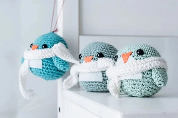 Three crocheted penguins sitting on a shelf.