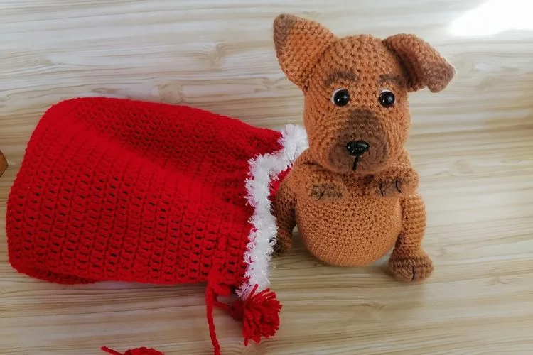 A crocheted dog wearing a red santa hat.