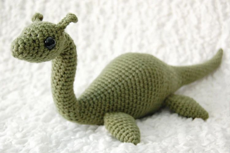 A green crocheted dinosaur laying on a white blanket.