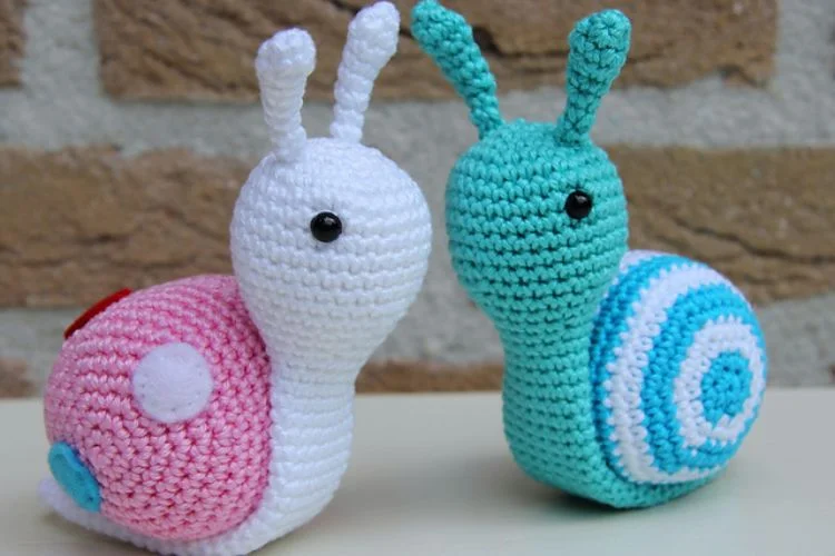 Two crocheted snails sitting next to each other.