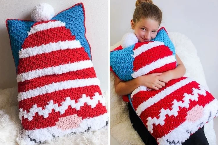 A girl is holding a crocheted pillow with a santa hat on it.