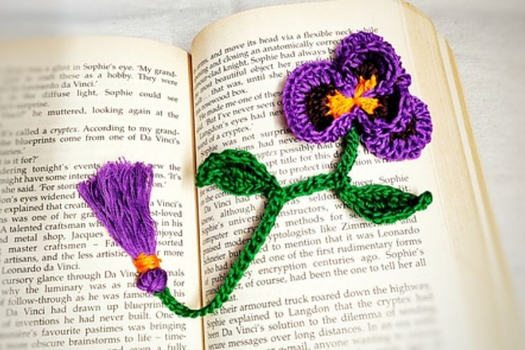 A crocheted pansy bookmark on an open book.